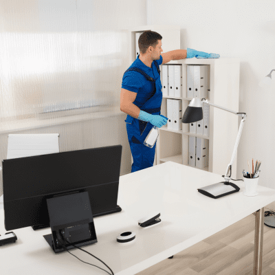 Office cleaner disinfecting shelves and office workspace